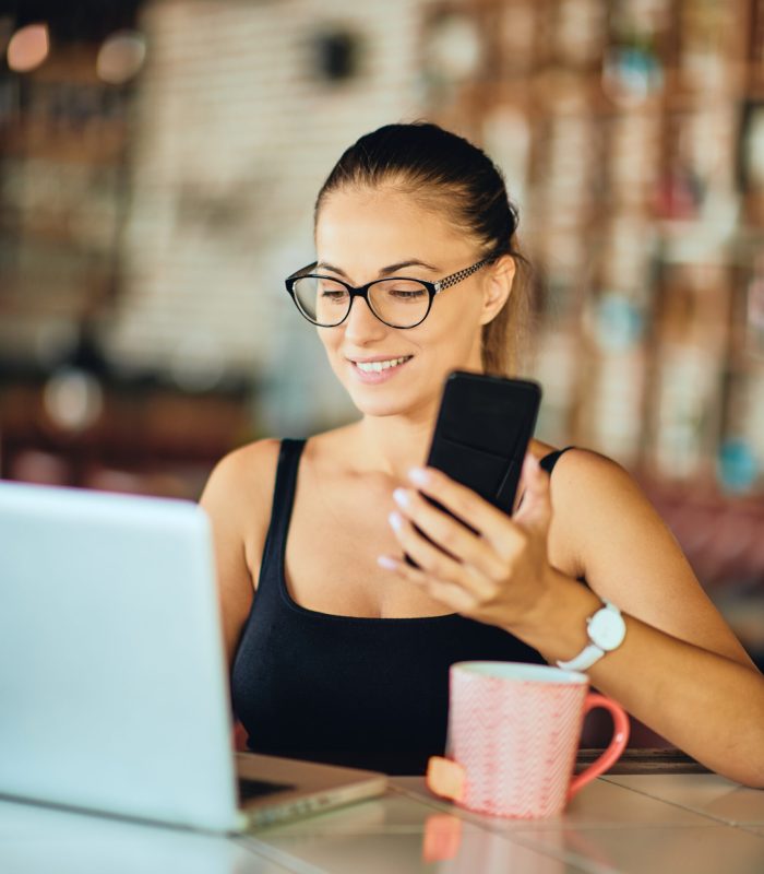 Caucasian,Woman,Using,Smart,Phone,And,Laptop,While,Sitting,In